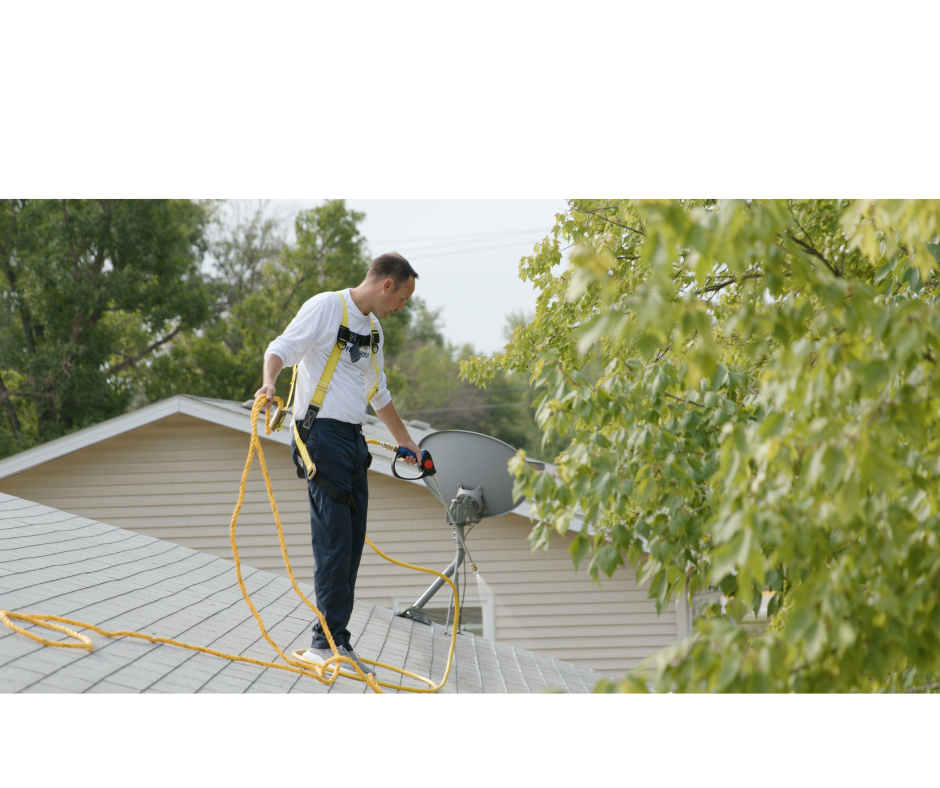 Roof technician with safety harness applying treatment to a residential roof